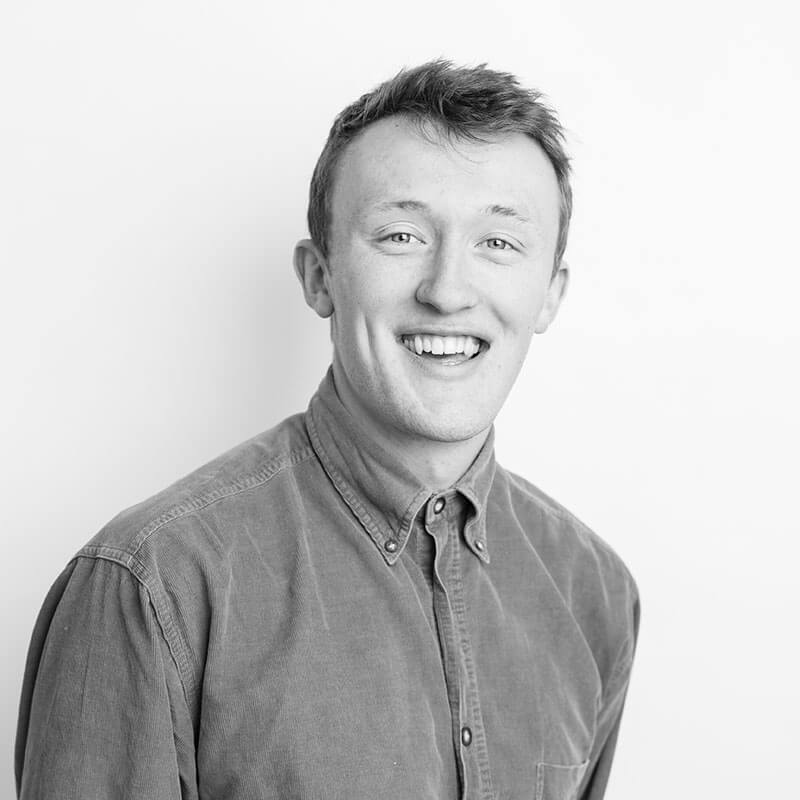 Greyscale headshot of a man smiling at the camera. He has short light hair and is wearing a shirt.