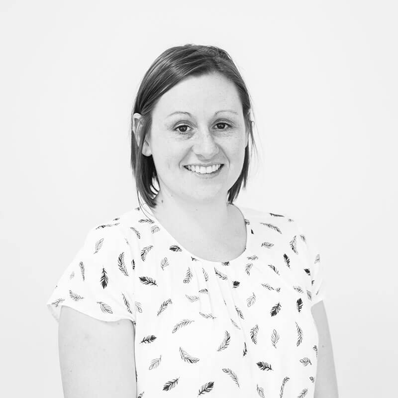 Greyscale headshot of a woman with short brown hair. She is smiling at the camera and is wearing a patterned white short-sleeved top