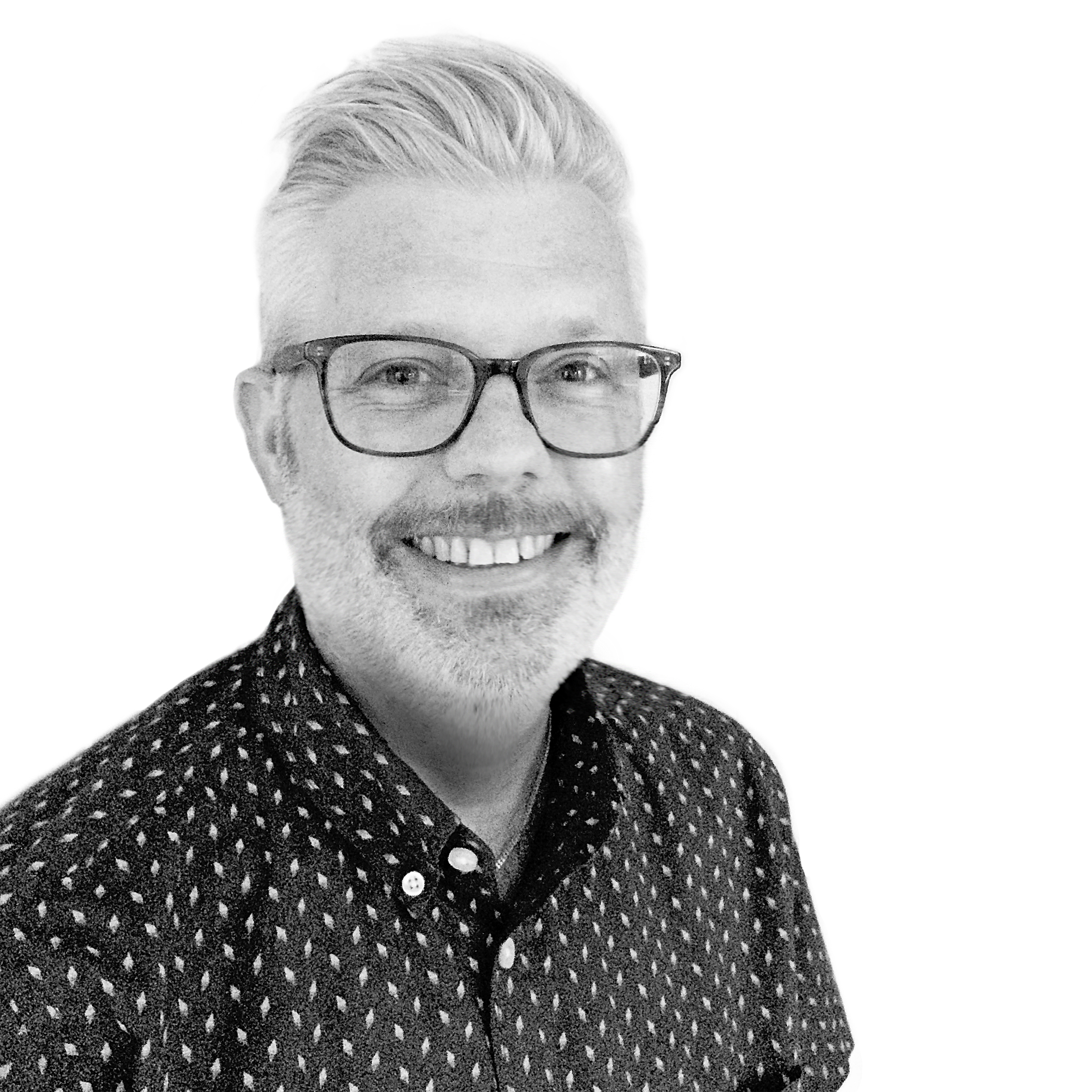 Greyscale headshot of a person with light, short hair, glasses with black frames, and stubble. He is smiling and wearing a black spotted shirt.