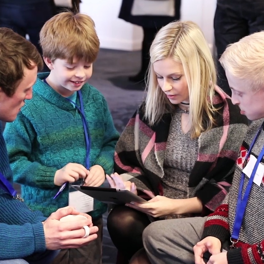 Four people crowded round a tablet that's held by a blonde haired person in the centre of the group