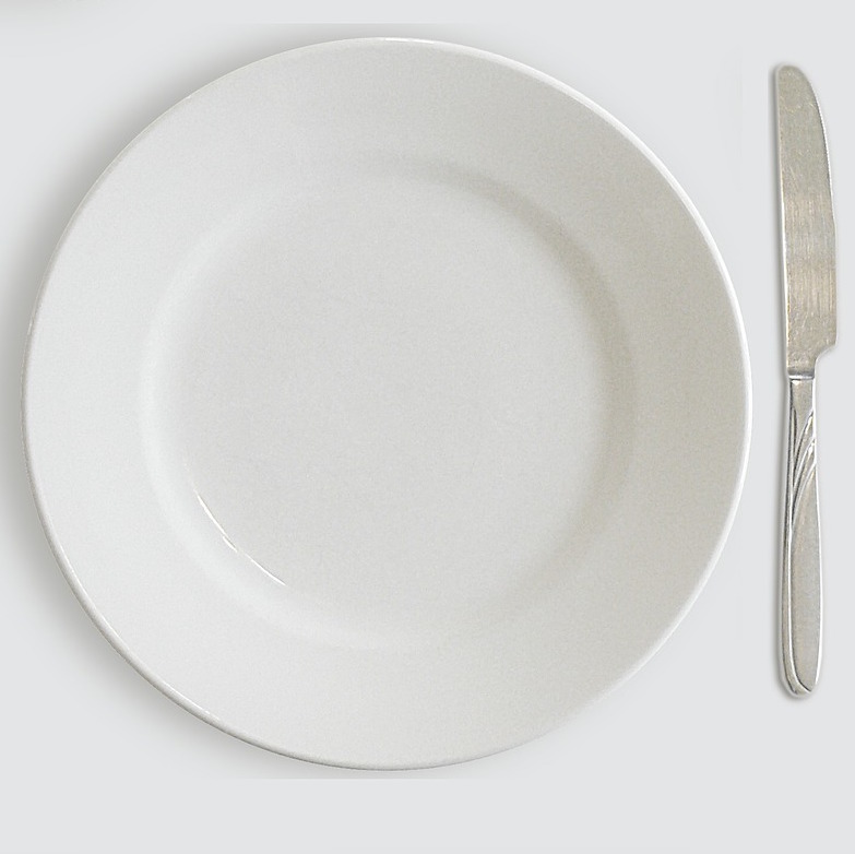 Photo. An empty white plate sits on a white background. A silver knife sits to the right of the plate.