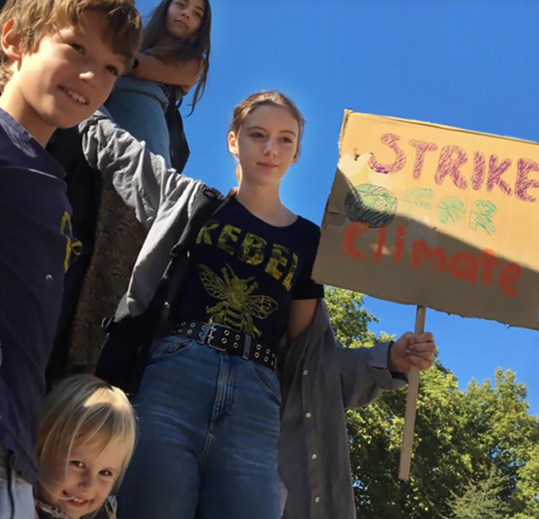 A group of young people holding a cardboard banner that has Strike written on it. There's blue sky behind them.