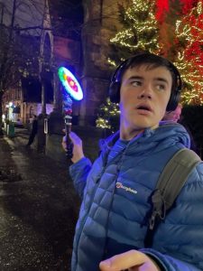 A young person with headphones on and wearing a blue quilted jacket. There are bright lights around them