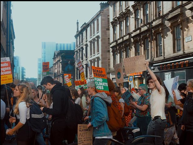 Photo of a protest, with lots of people holding signs that relate to the climate crisis and Trident. They are outside on a street in Edinburgh