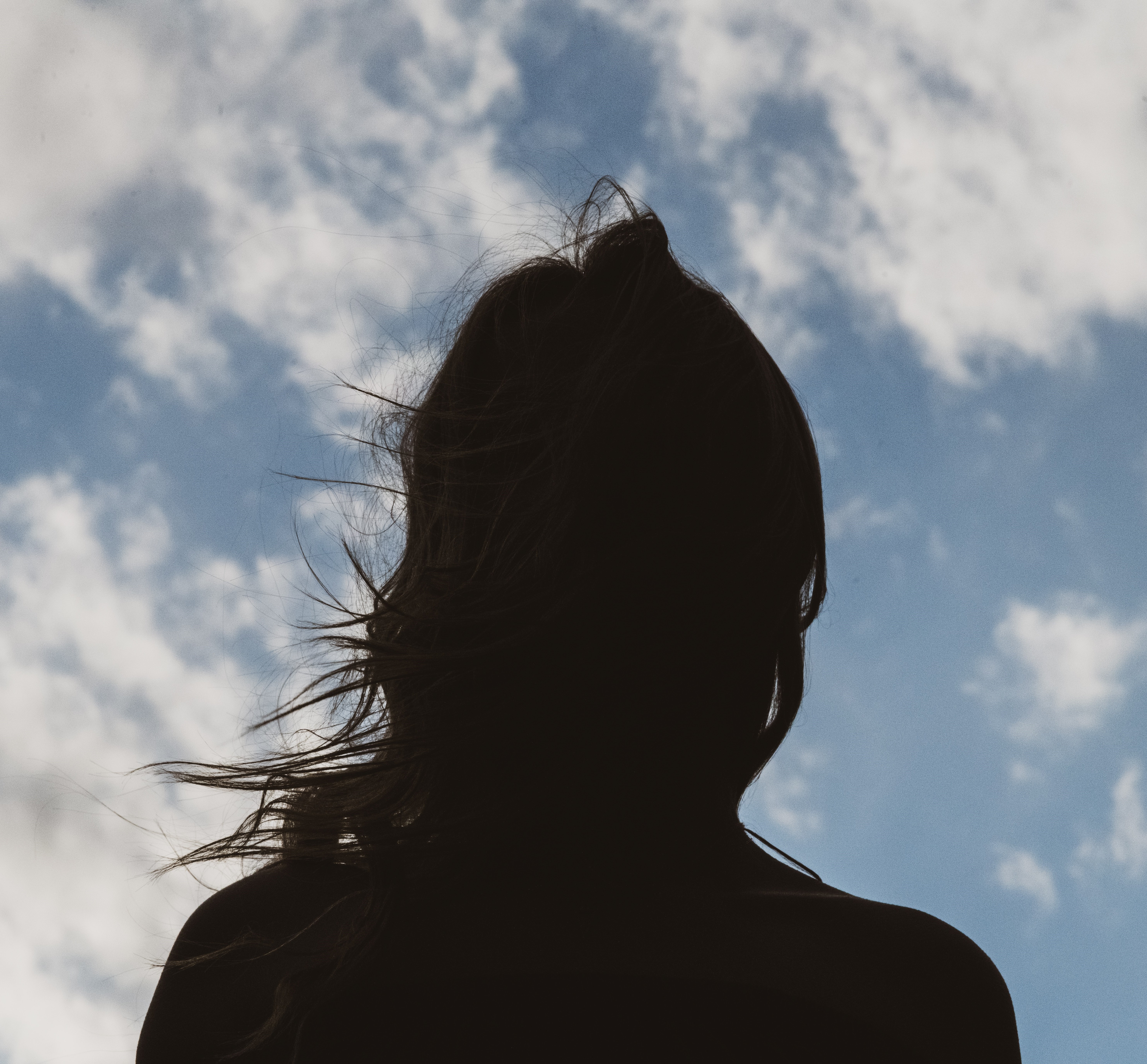 Silhouette of a person with long hair looking at a blue sky with clouds