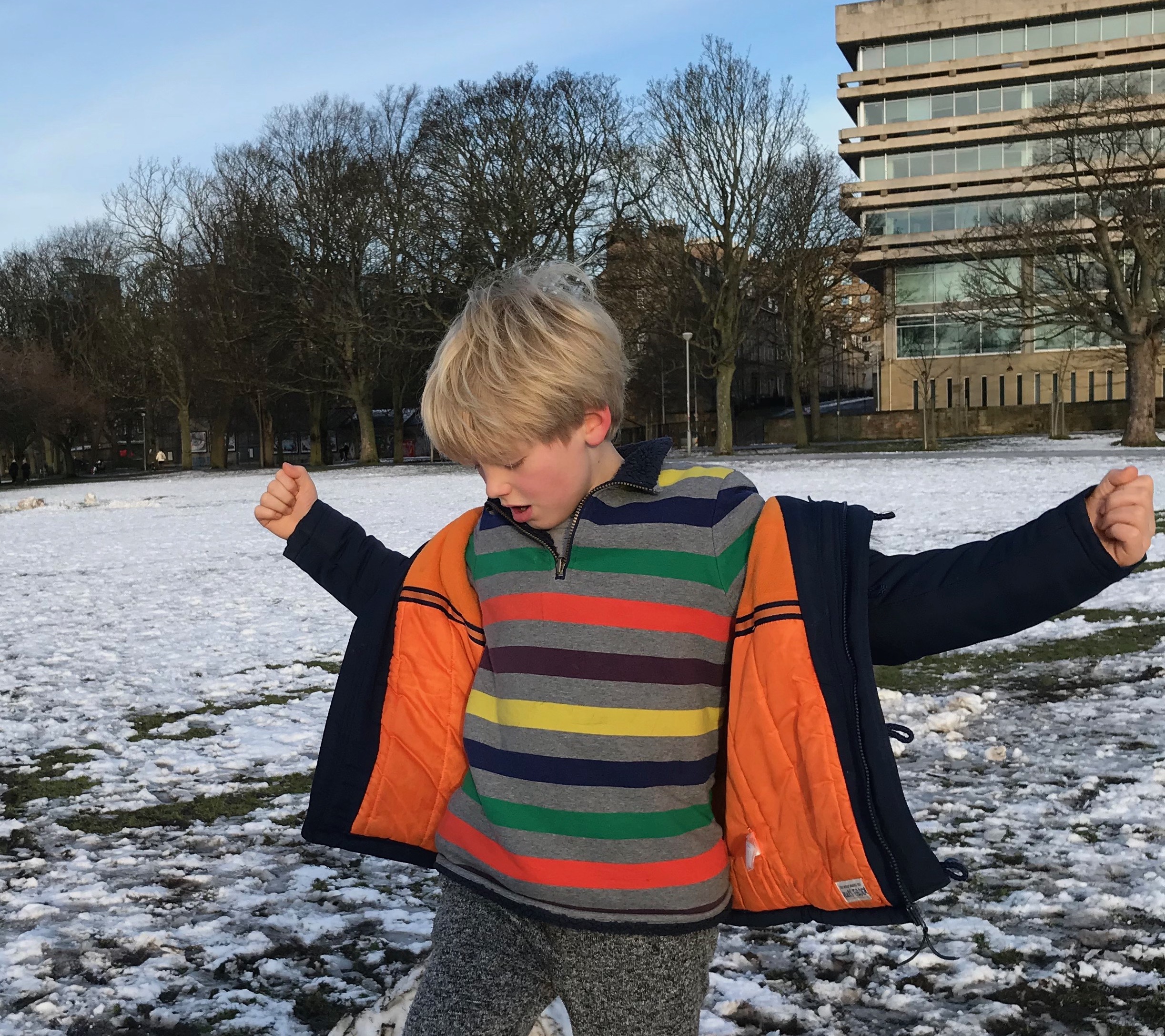 Boy with blond hair playing in the snow with his arms outstretched