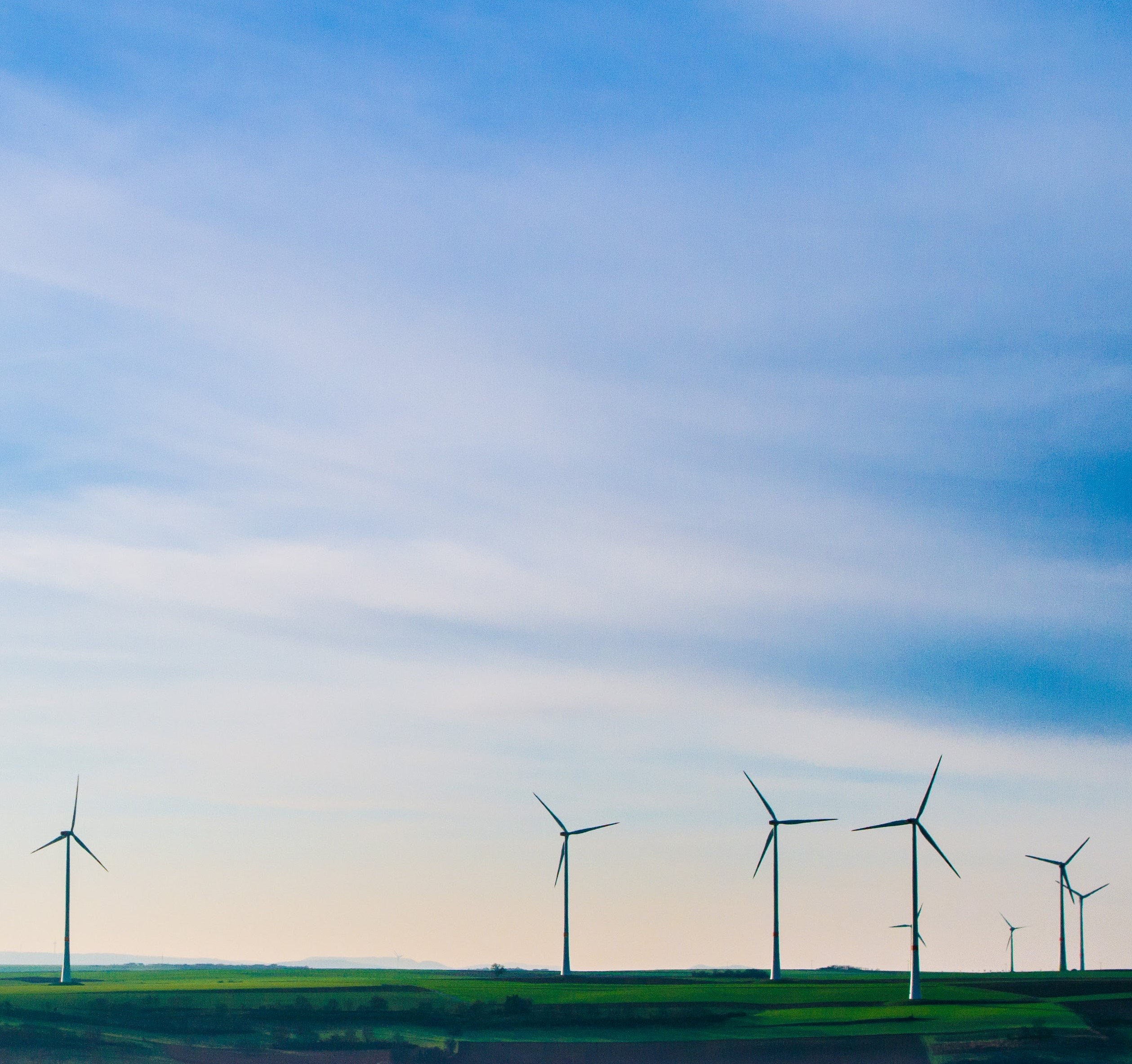 Wind turbines on green fields, with a large blue sky with clouds above them.