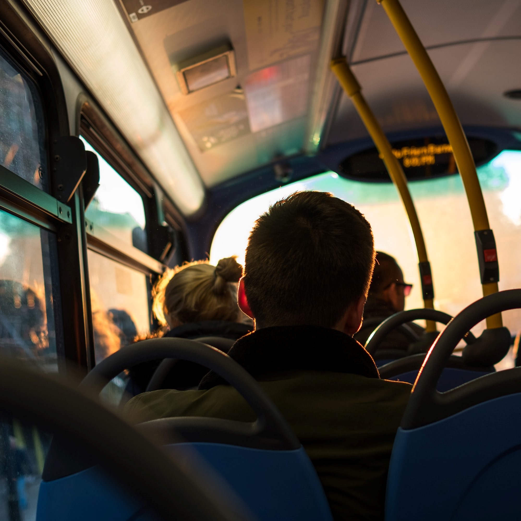 A photo on a bus, with a person's head in the foreground as people are sitting on the bus seats.