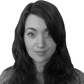 A black and white image of a woman above her shoulders. She is looking at the camera and has long dark wavy hair