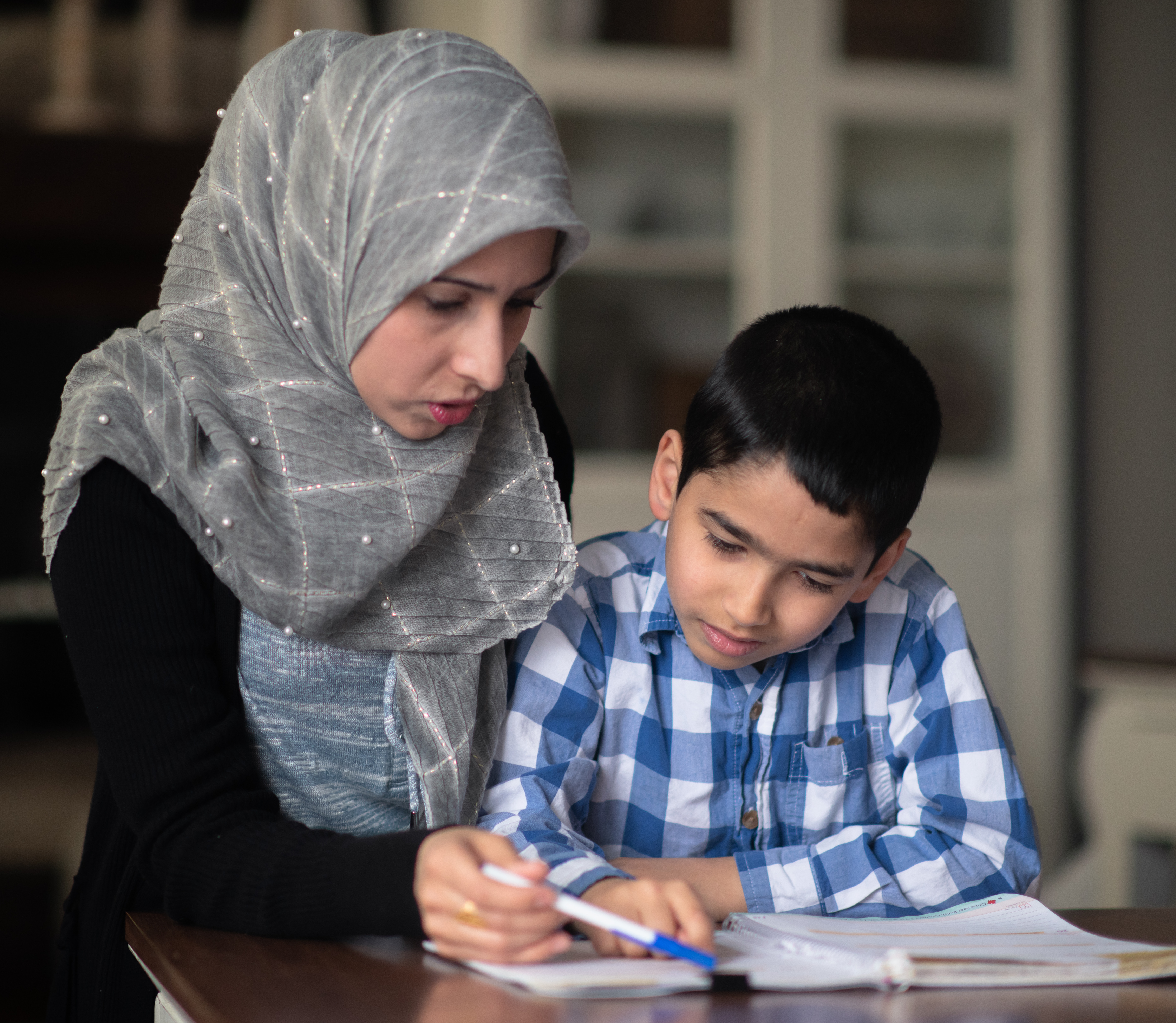 A middle eastern woman is helping her son with his school work in their living room at home.