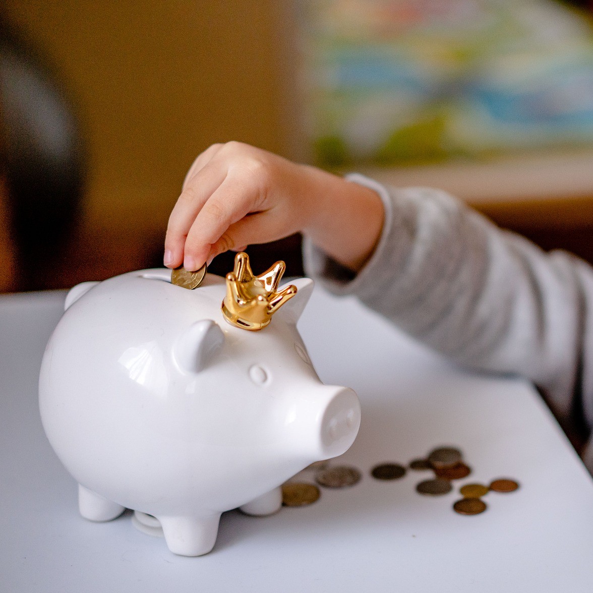 A child reaching to put coins into a piggy bank