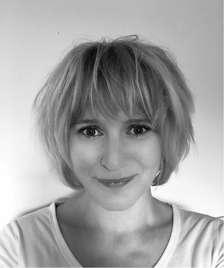 A black and white photo of a woman from the shoulders up. She is wearing a light coloured top and her hair is in a light choppy bob, with a fringe over her forehead. She is looking at the camera and smiling without teeth showing.