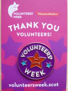 A purple enamel badge that says Volunteers Week 1-7 June with a red star on it. On the surrounding card it says 'thank you volunteers!' volunteersweek.scot
