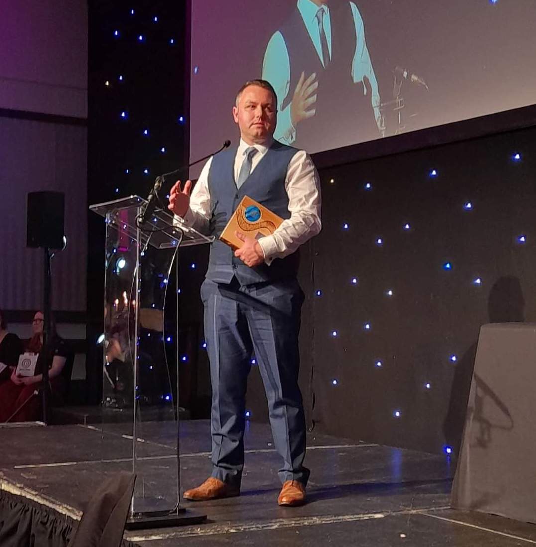 A man in a suit stands on a stage accepting an award