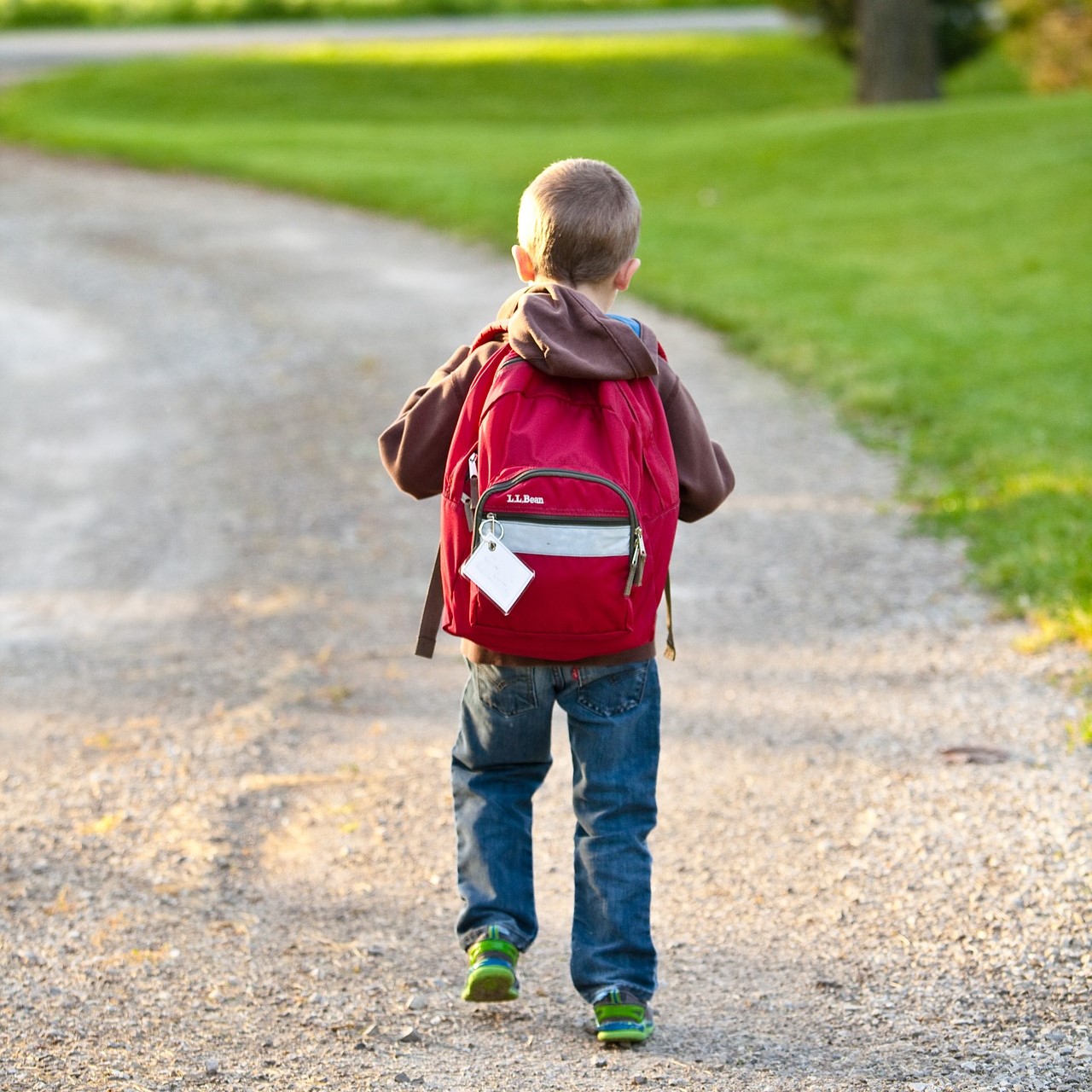 Photo of young child walking away from the camera, with a school bag on their back