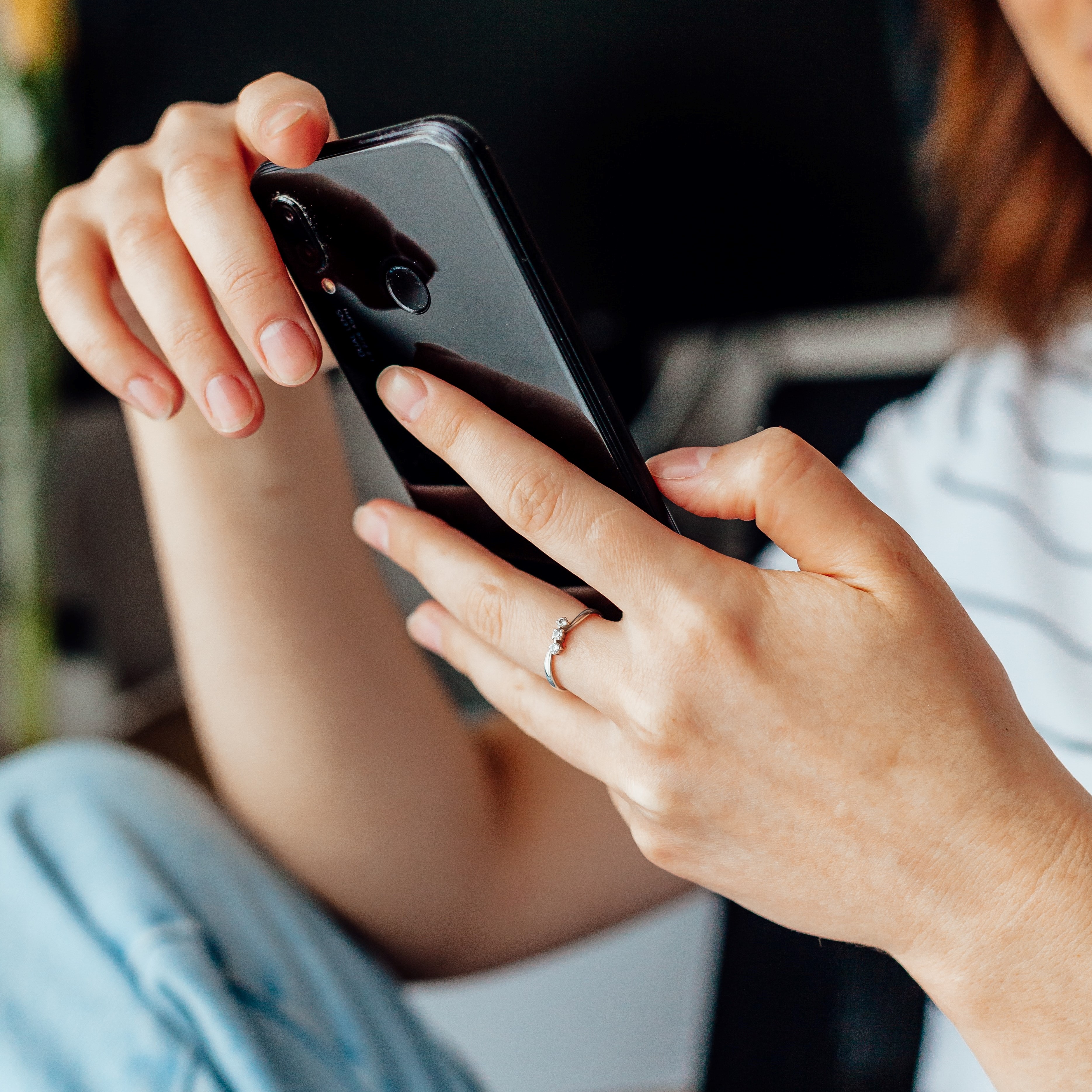 Two hands holding a smart phone, the person is out of focus looking at the screen