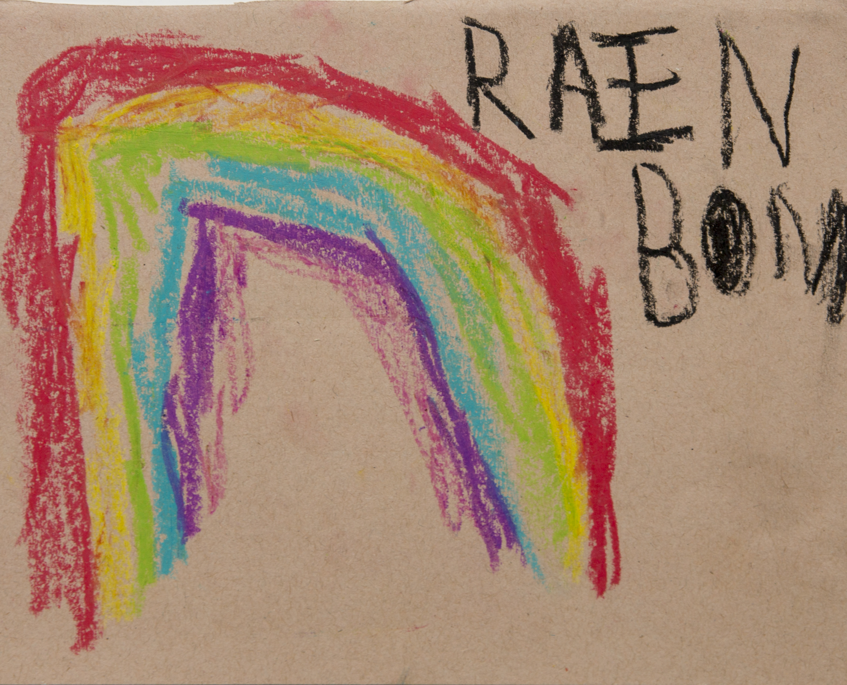 A children's drawing of a rainbow using crayons on brown paper . The rainbow uses red, yellow, green, blue and purple. The word rainbow is written in the top right corner in children's handwriting, using black crayon.