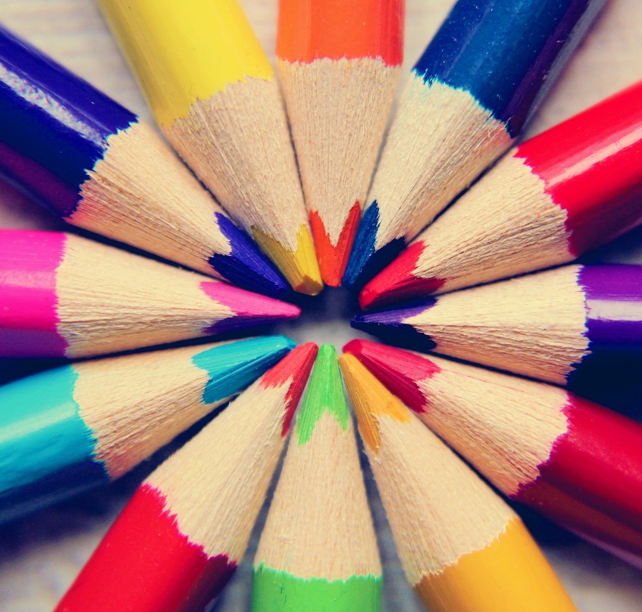 Coloured blue, red, purple, yellow, green, orange and pink pencils arranged with their nibs all pointing together, forming a circle.