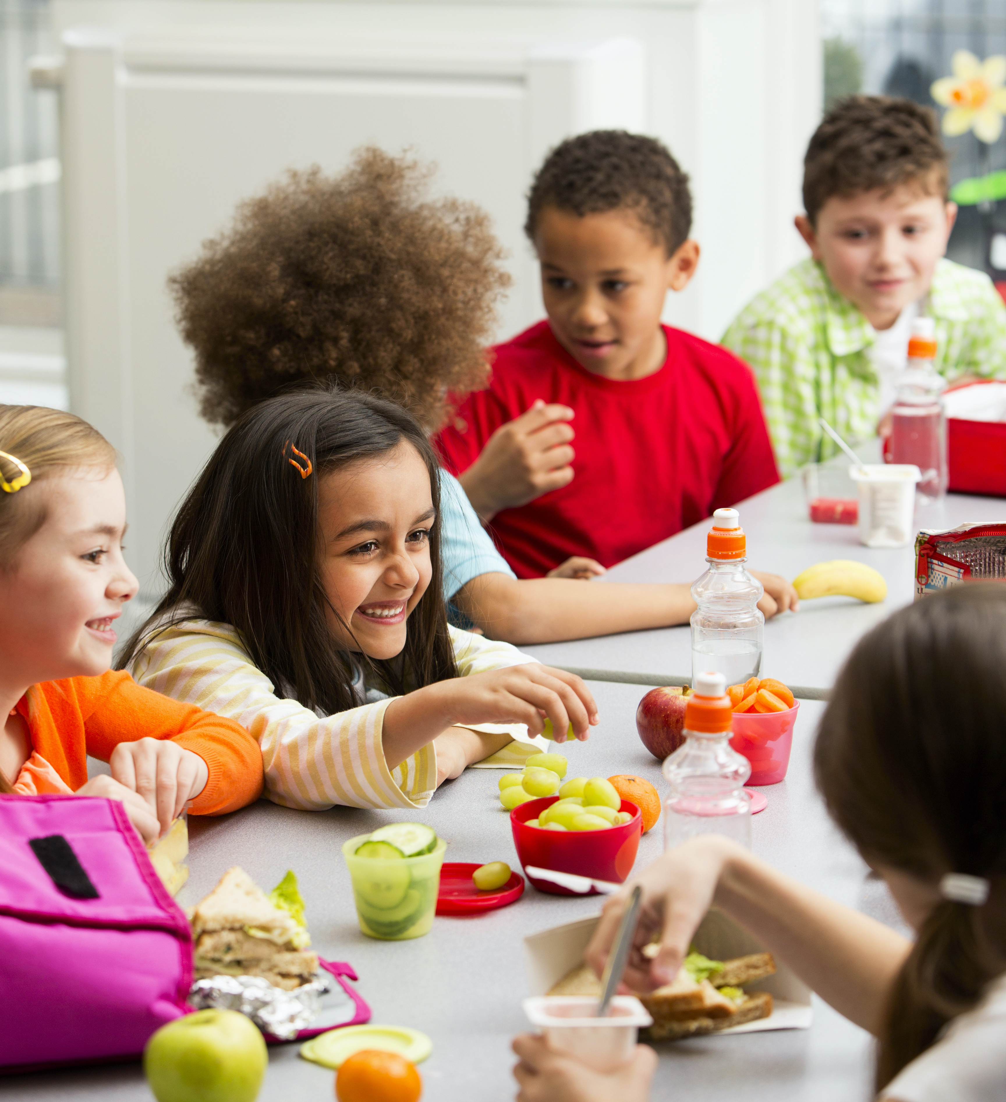 Children sitting at a table at school and enjoy their packed lunches together