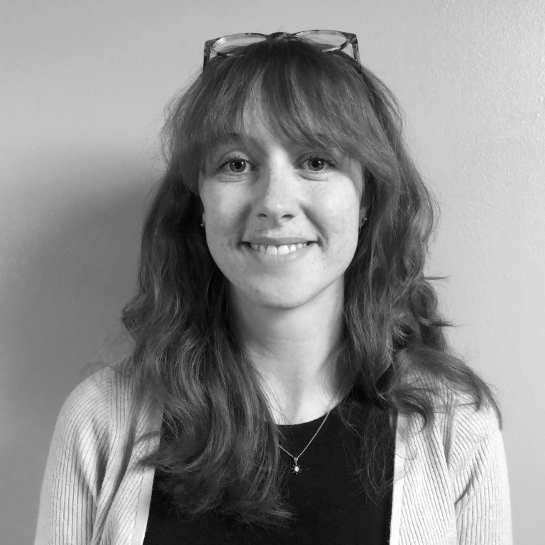 A black and white image of a smiling person with glasses on their head and long wavy hair