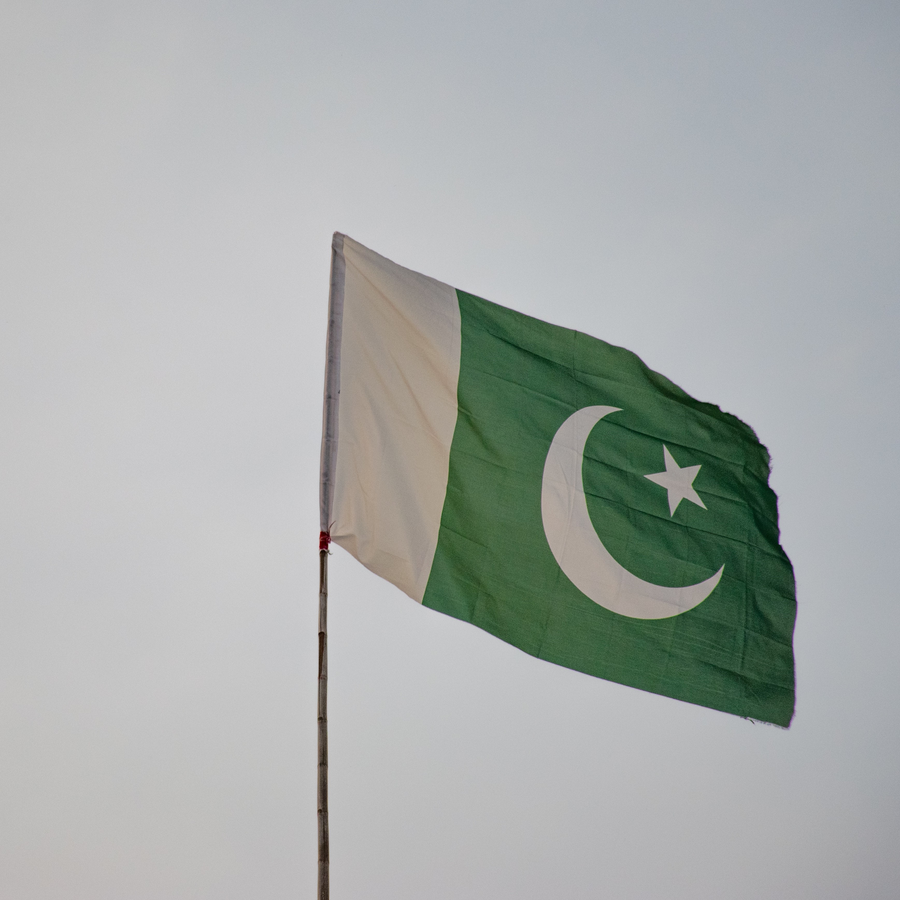 Pakistan's flag flying with a grey sky background. The flag has a white strip on the right, with a moon and star on a green background on the right.