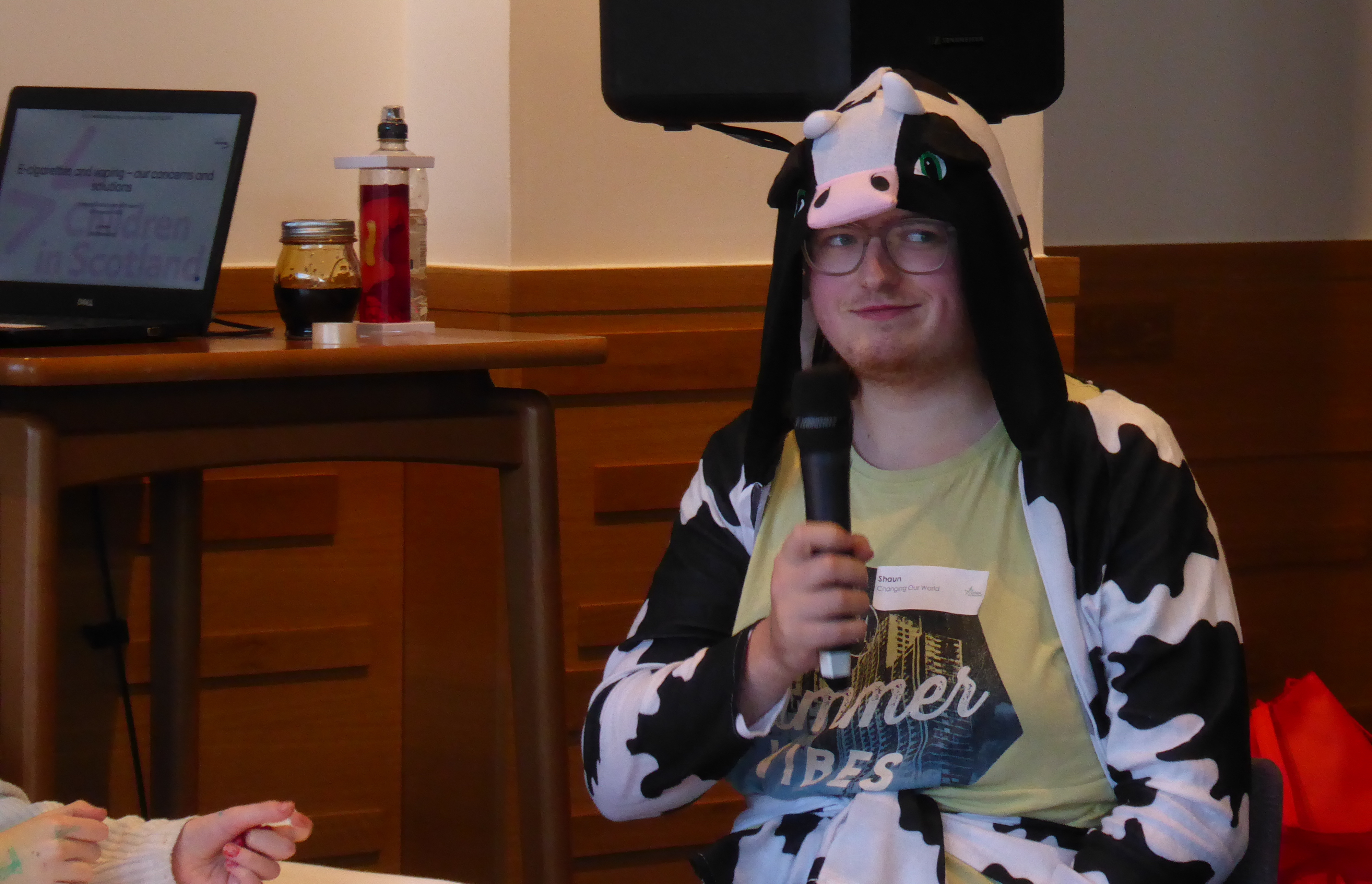 A young person wearing a cow costume, holding a microphone.