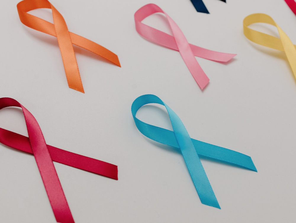 Photo. A number of different cancer awareness ribbons are laid out on a white background, including a red ribbon, blue ribbon, orange ribbon and pink ribbon.
