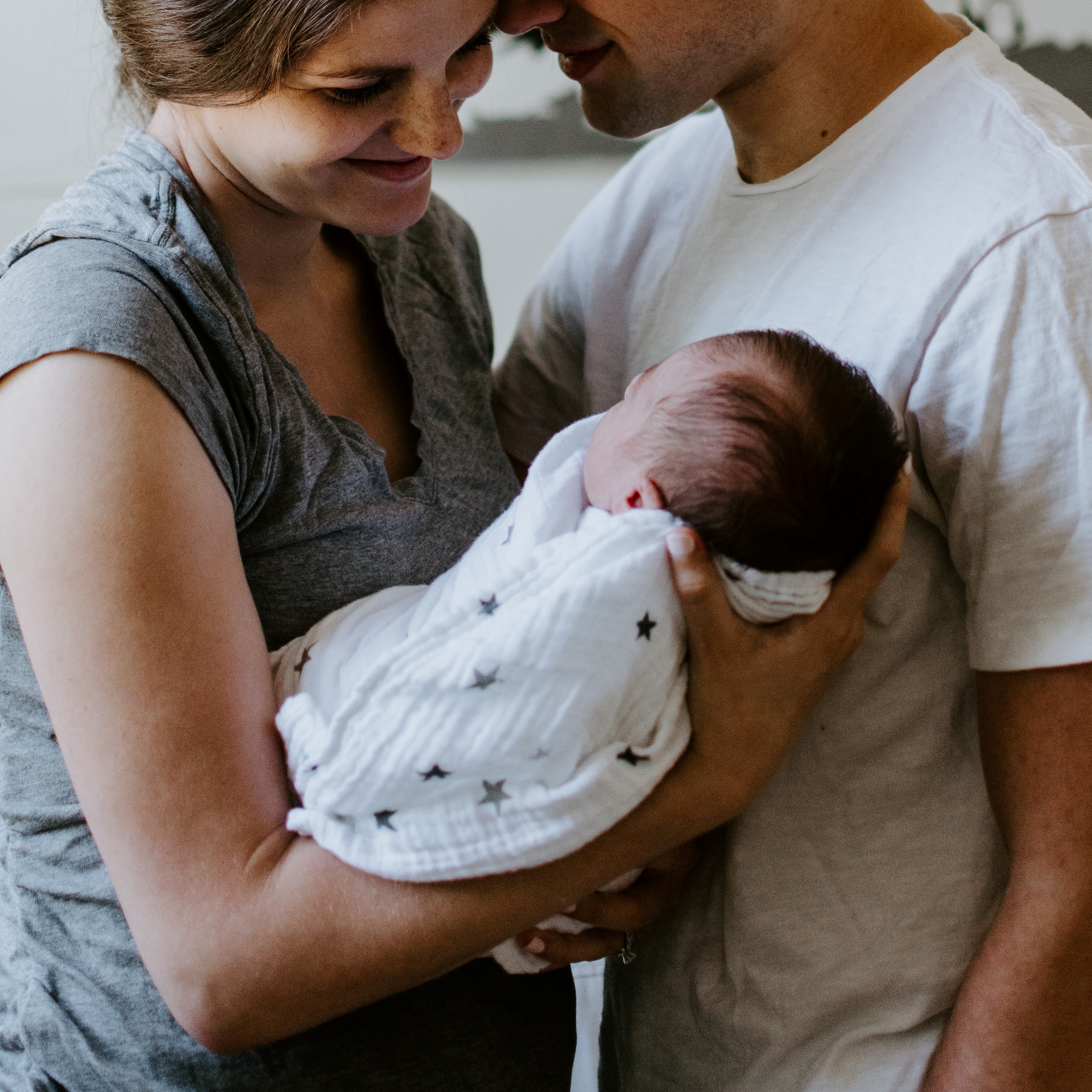 A newborn baby being held by their mother. She is looking down them with the father nearby.