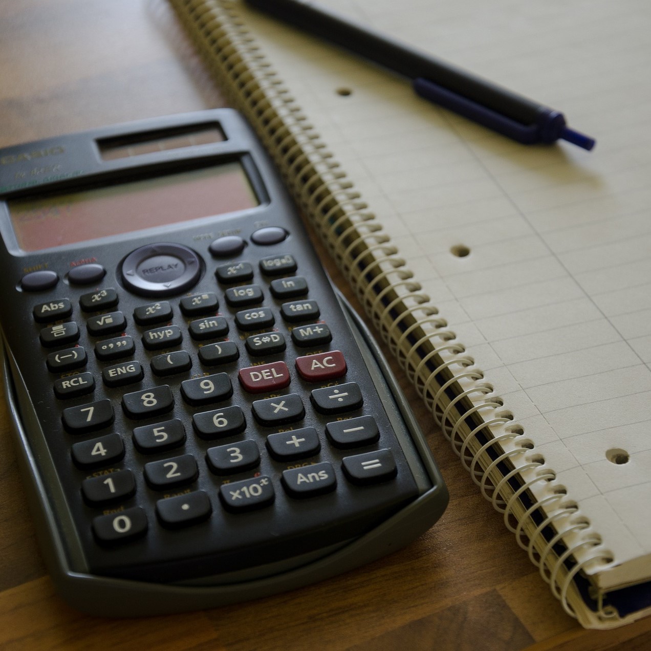 Photo of a calculator next to a lined notepad with a pen on it.