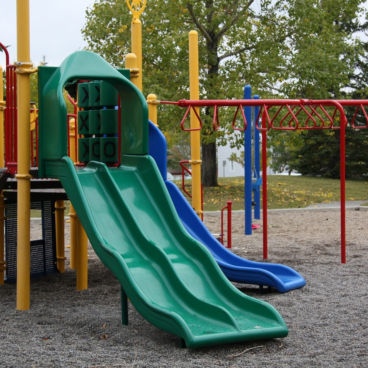 An outdoor play park, with a green slide, red monkey bars and yellow pillars.