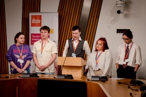 Colour image of five young people from the Fostering Network's Young Advisory Board speaking at the Scottish Parliament