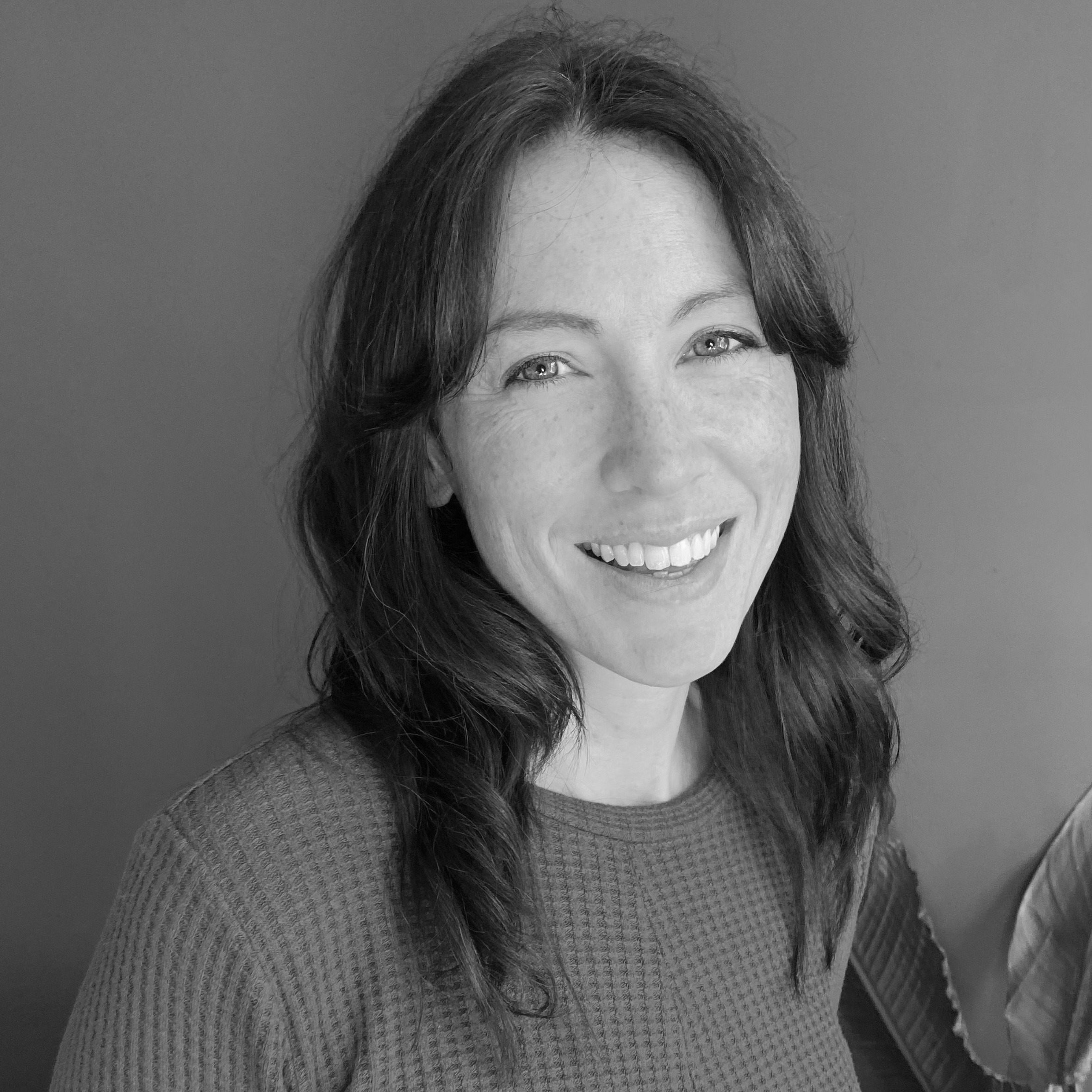 A greyscale image of a smiling person with long dark hair
