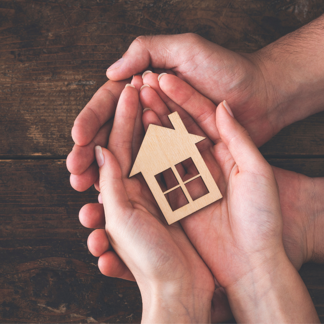 Two sets of hands hold a wooden sculpture of a home