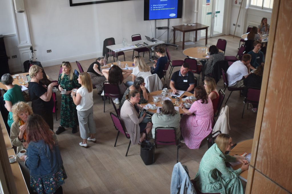 A large room full of people standing or sitting at big tables.