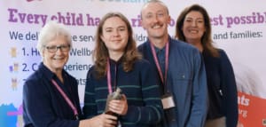 Four people wearing red lanyars stand together holding a silver trophy