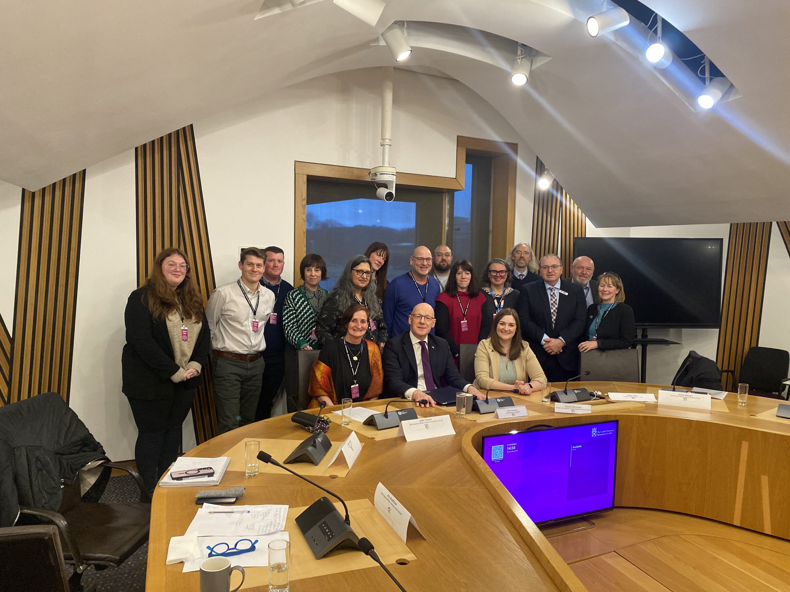 A group of people stand behind a large wooden desk. 