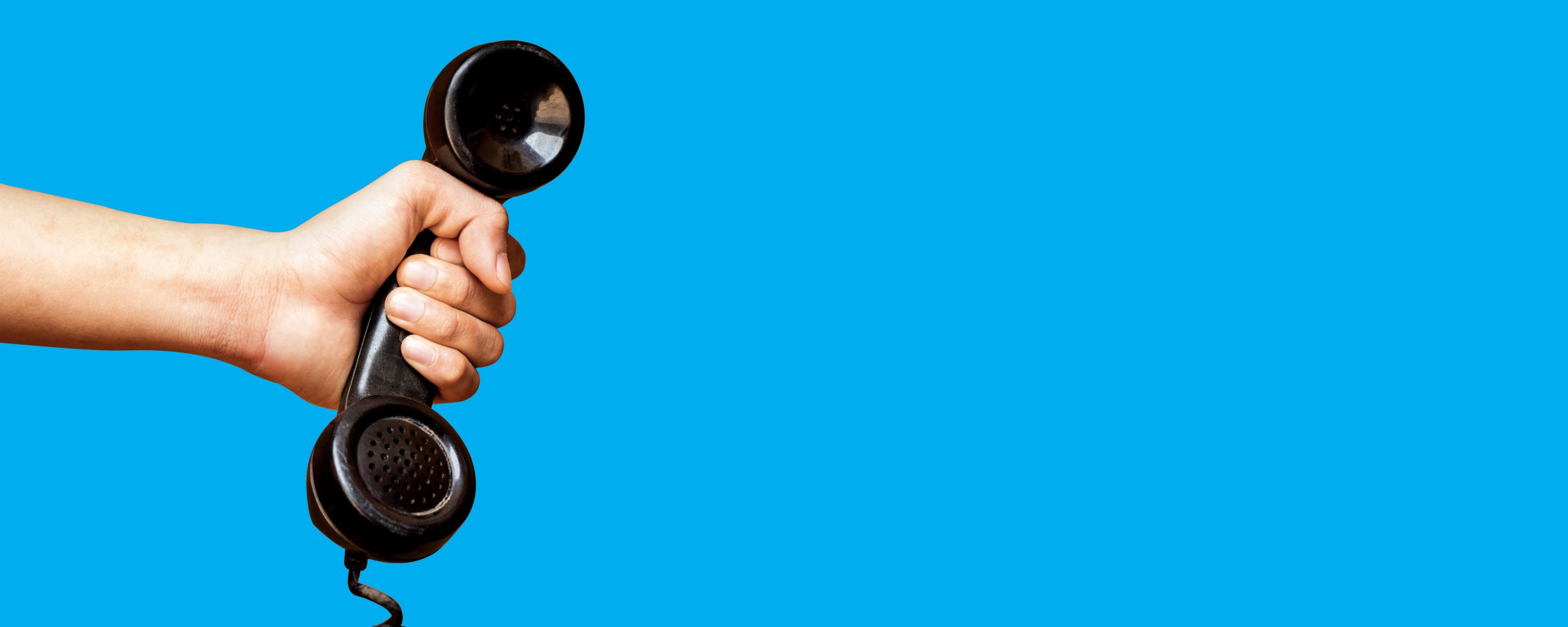 Hand holding old telephone receiver on blue background.