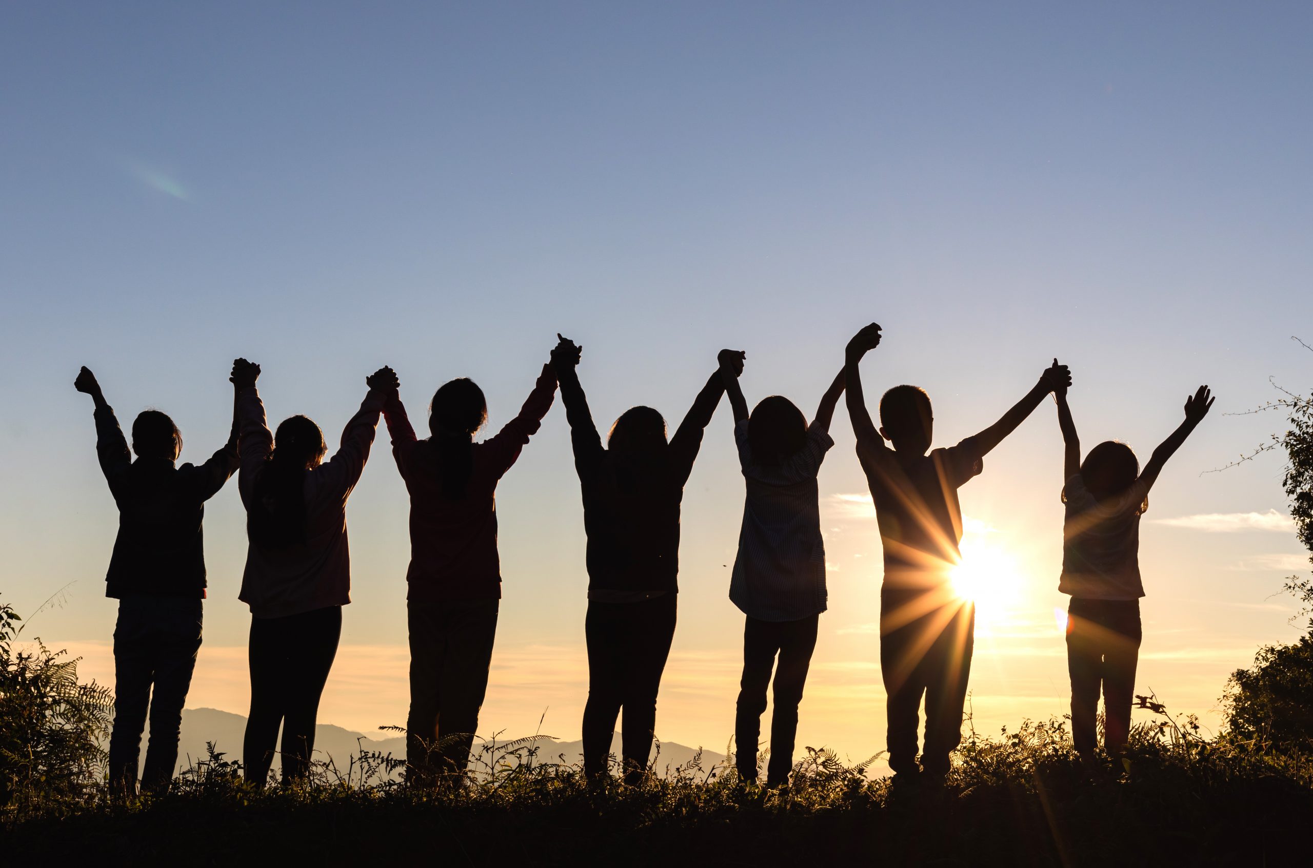 Silhouette of happy children standing with raised hands on the mountain at the sunset time.