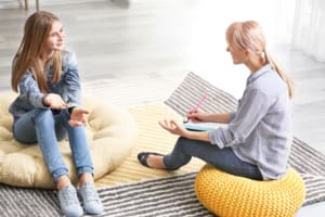 Female psychologist holding clipboard and talking with teenage girl in office
