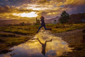 Girl jumping over a stream on the Isle of Arran at sunset during winter