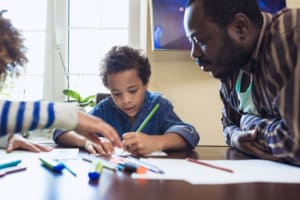Father overseeing the homework of his two children at a dining room table