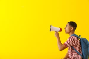 Teenage boy with megaphone against bright yellow background
