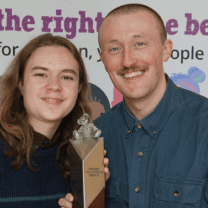 Two smiling people stand holding a silver award