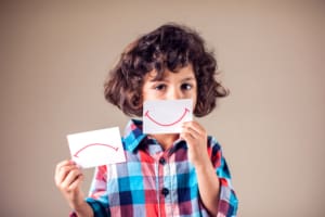 Boy selecting between positive and negative expressions drawn on paper and held in front of face