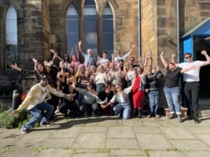 A large group stand it front of a church with arms raised in the air in celebration