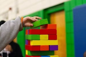 Teenager's hand placing a colourful Jenga block at the top of the tower