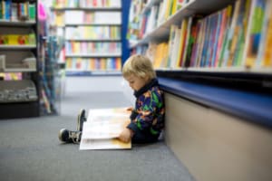 Young boy sitting on the floor of a library with a book open across his legs