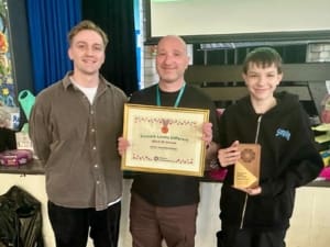 Three smiling people, with person at the centre holding a certificate