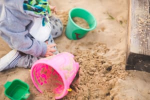 Young child playing in a sandpit with colourful buckets