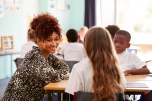 Primary school teacher helping pupils wearing uniform as they work at desk in classroom